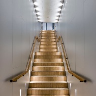 Un escalier recouvert de parquet mène à l’étage supérieur et se distingue de manière remarquable par rapport à la blancheur des murs et des plafonds.