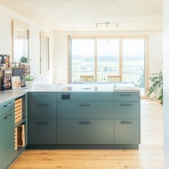 La cuisine moderne aux façades gris-vert est ouverte sur la salle à manger avec balcon.