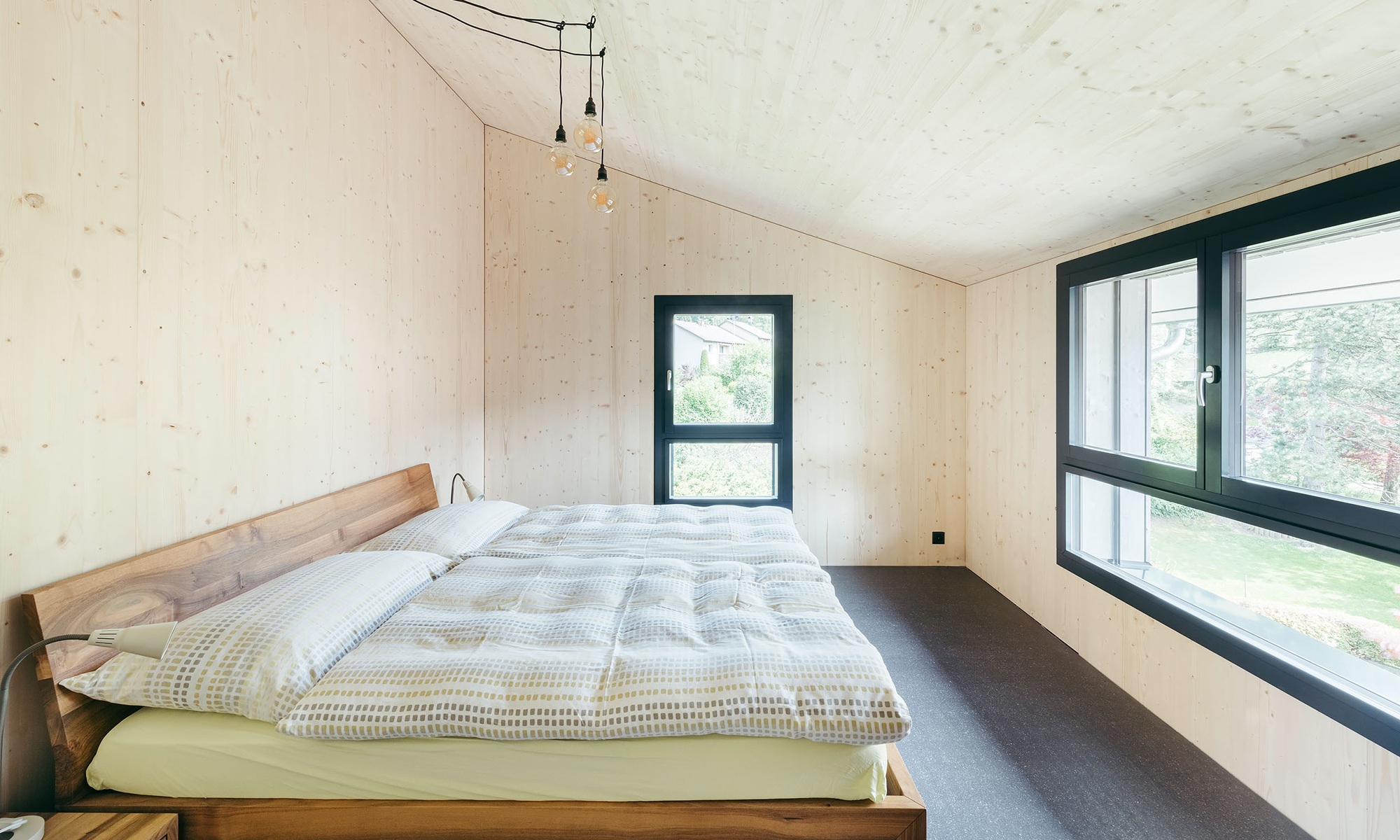 Innenansicht Schlafzimmer mit Holzbett, einer langen Fensterfront und einem schmalen Einzelfenster
