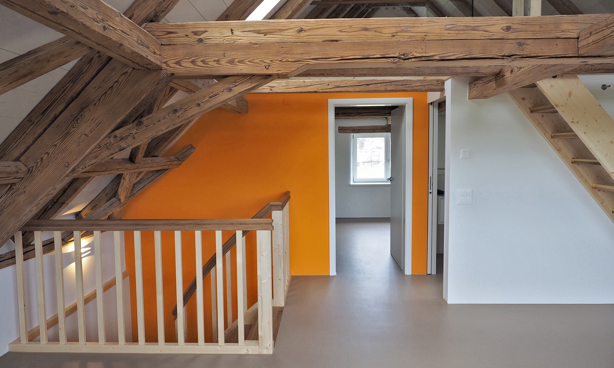 Aufnahme zeigt das grossräumige Dachgeschoss mit Zugang zu weiteren Zimmern, zwei komplett aus Holz ausgestatteten Treppen und den breiten Holzbalken.