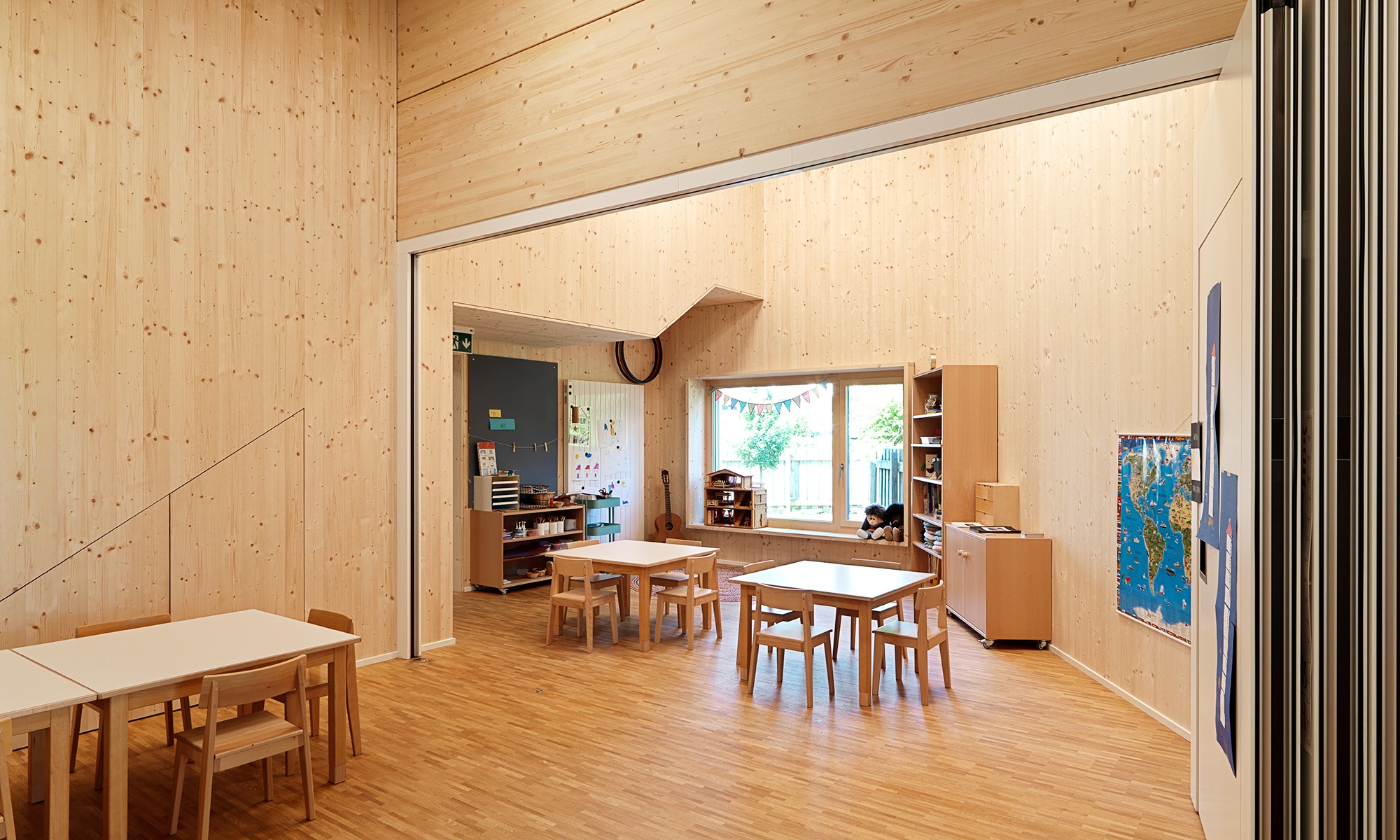 Innenansicht des Klassenzimmers im umgebauten Kindergarten Wittenbach. Wände, Boden und Decke des Zimmers sind aus Holz. Mit einer Faltwand lässt sich das Zimmer in zwei Räume unterteilen. 