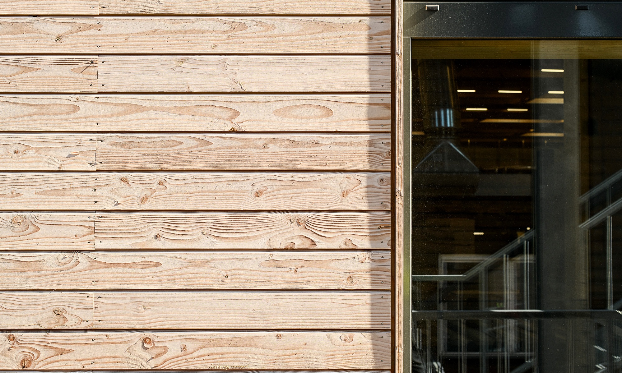 Detailansicht der Uvood-behandelten horizontal verlegten Holzfassade. Daneben der Ausschnitt einer Fensterscheibe. 