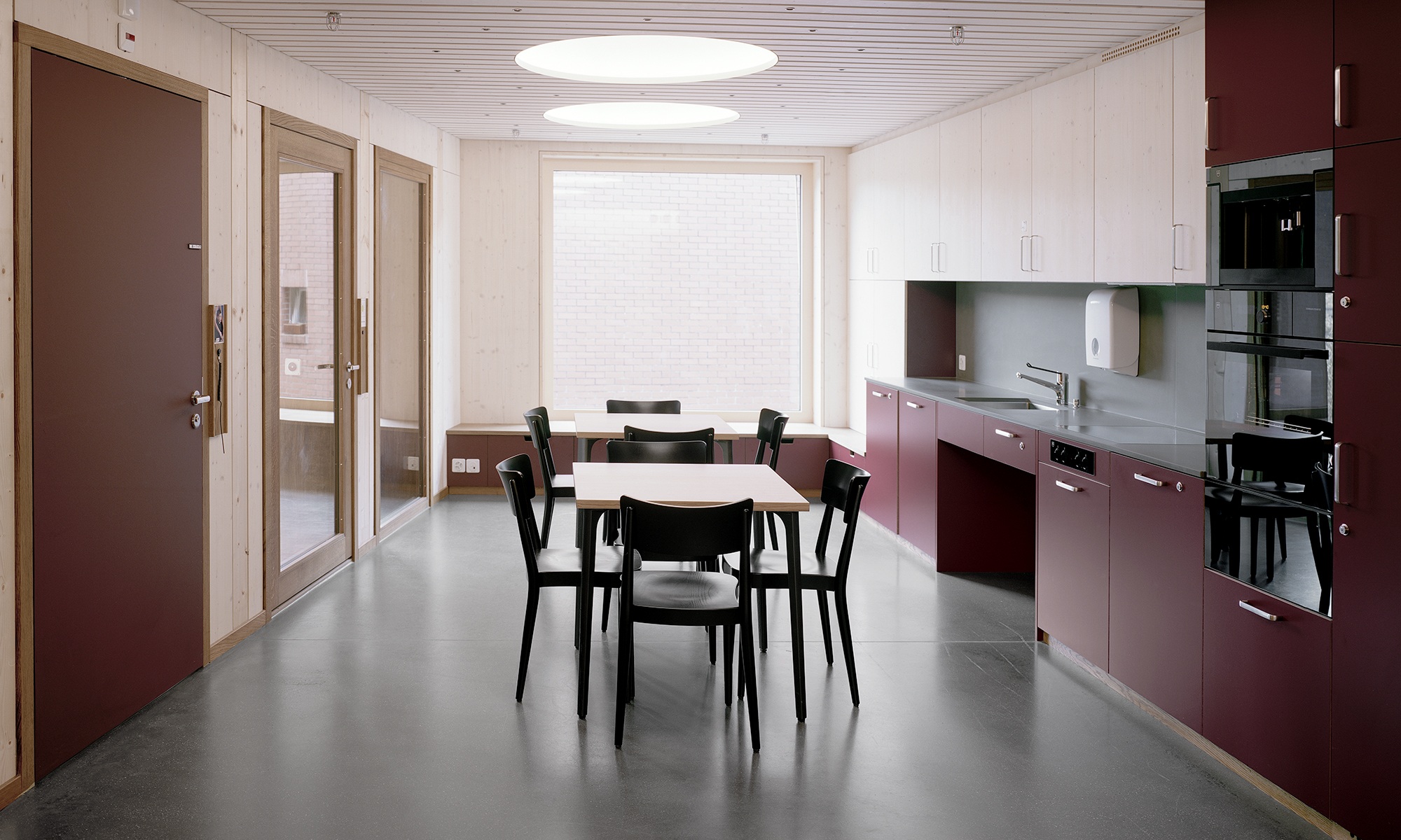 Innenansicht einer Küche im Wohnheim mit Wänden, Decke, Boden aus Holz und dunkelroter Küchenkombination