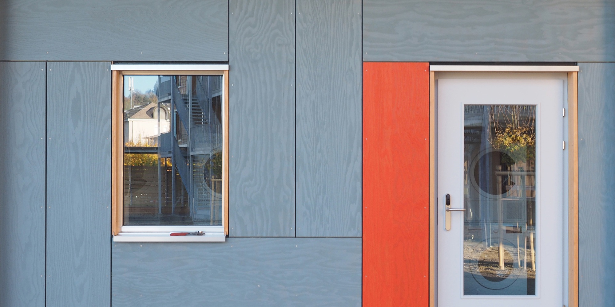 Aufnahme der grau sowie rot gefärbten Fassade von Asylzentrum Grosshof mit Grossansicht von Fenster und Türe