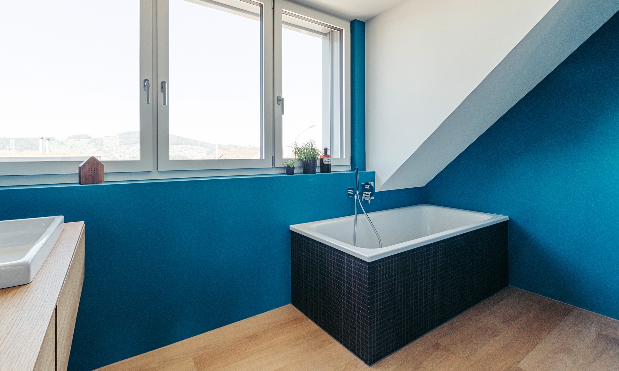 Gesamtansicht des Badezimmers mit blauen Wänden, Holzboden und grosser Fensterfront