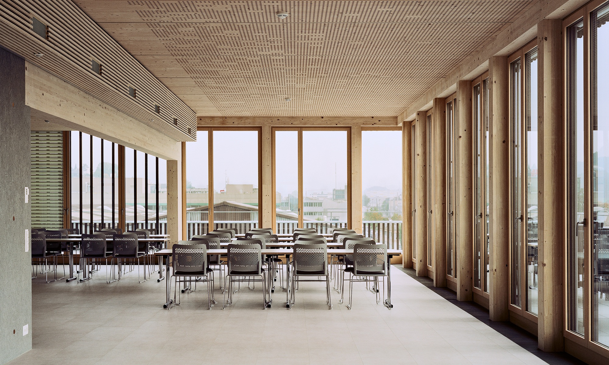 L’espace de détente est équipé de longues tables et de sièges. La pièce est baignée de lumière grâce aux baies vitrées, et les murs ainsi que la structure du toit sont entièrement réalisés en bois.