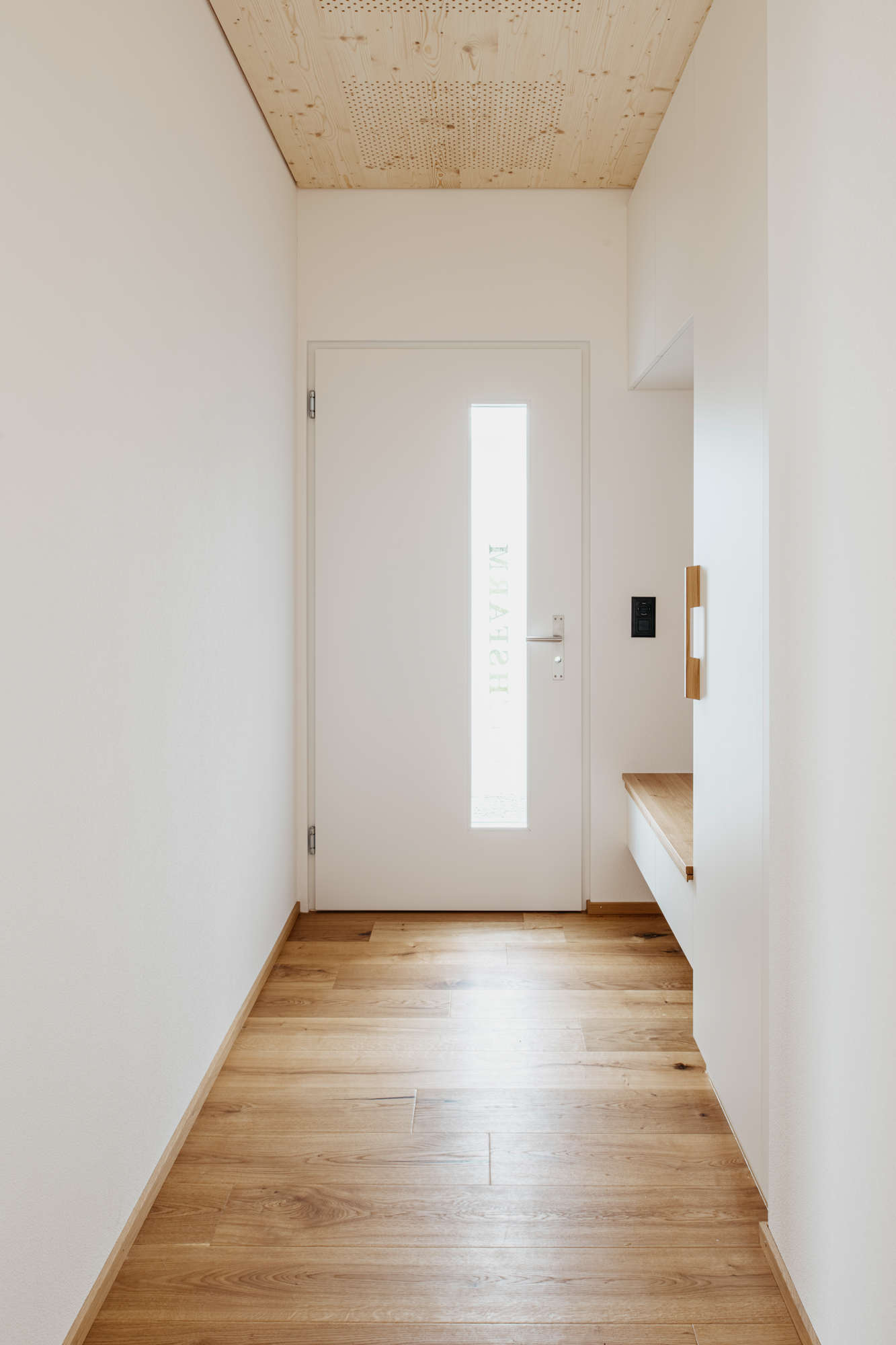 Entrée de la maison avec porte et murs blancs, plafonds et sol en bois.