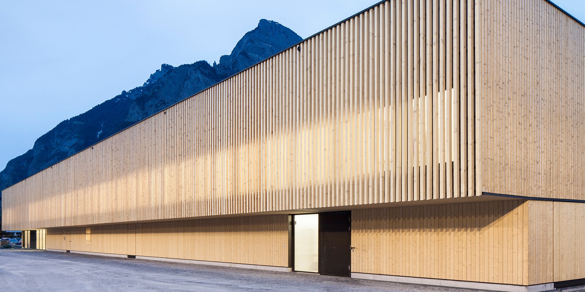The modern timber construction for RSA Sargans against a mountain backdrop at dusk.