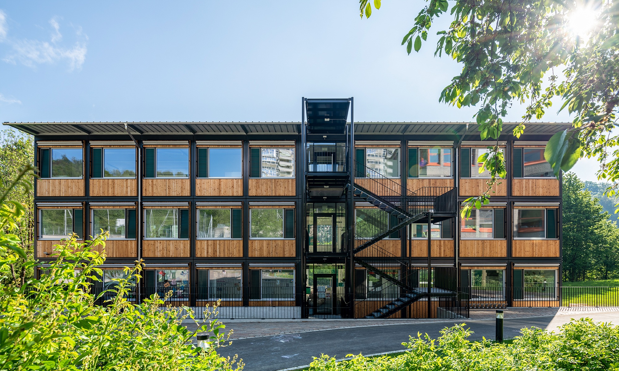 Gesamtansicht des ZM10-Schulpavillons Sihlweid in Zürich frontal von vorne, mit Pflanzen im Vordergrund