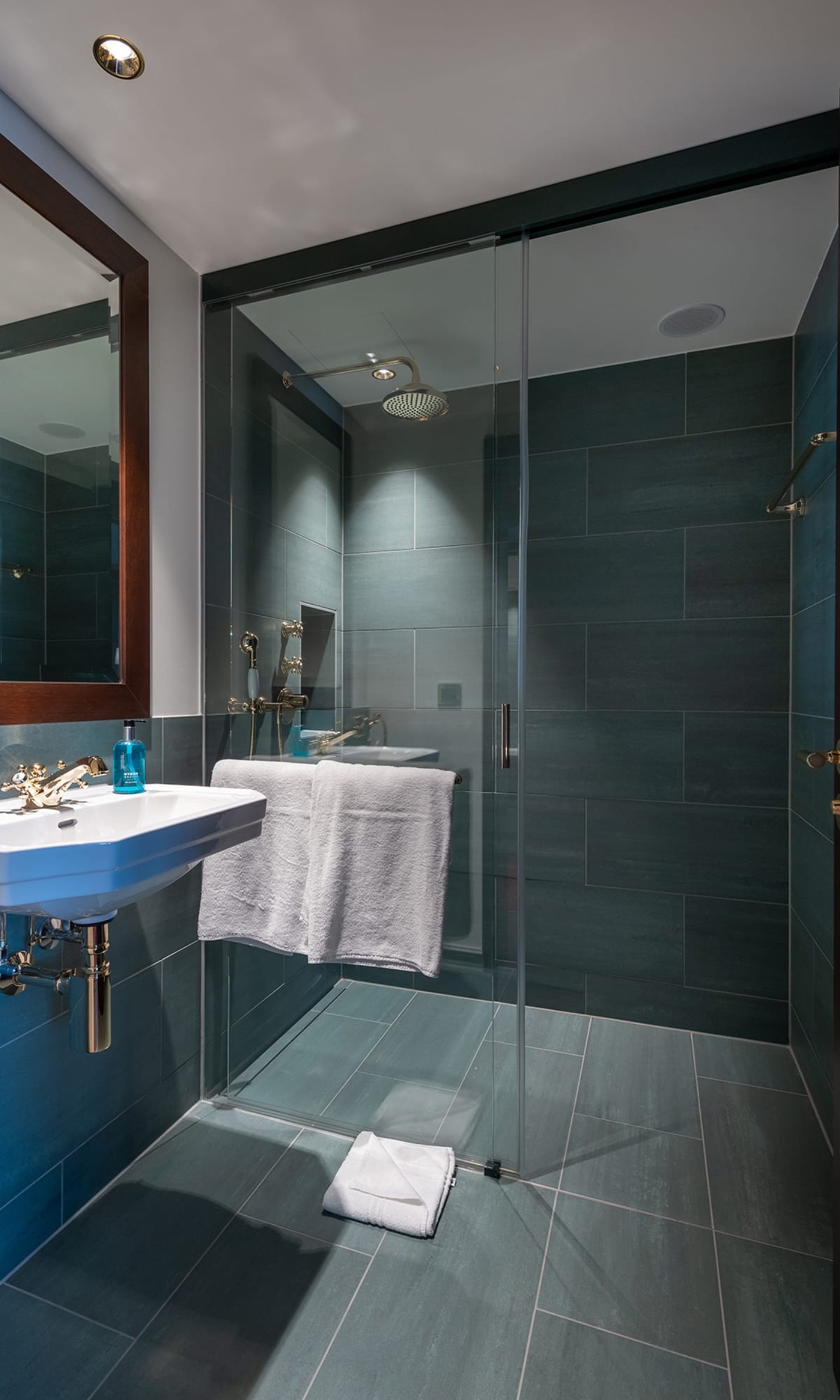 Douche dans le chambre d’hôte de l’hôtel Bad Horn, avec carrelage gris, porte vitrée et lavabo blanc 
