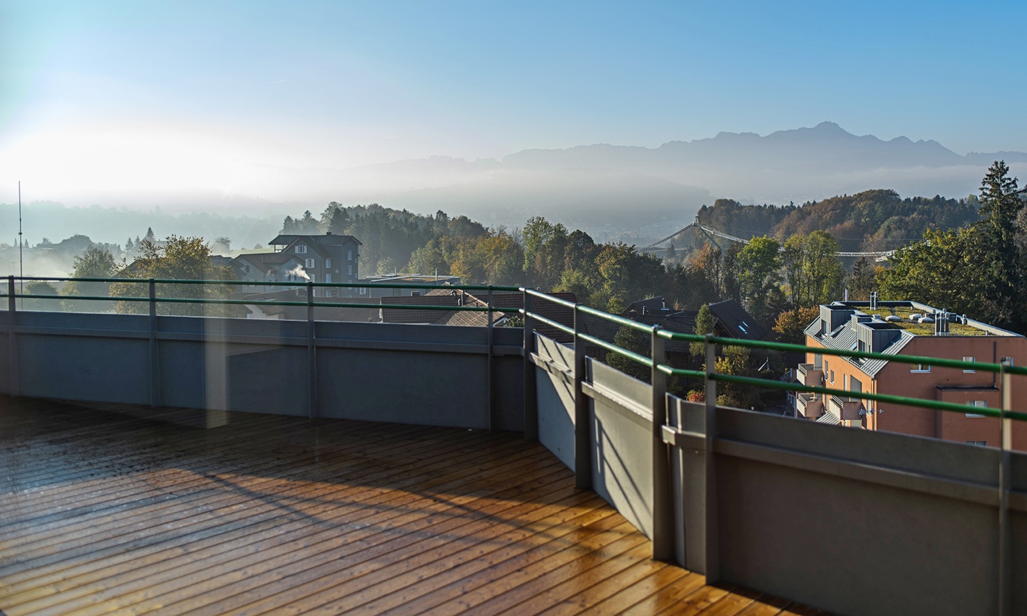 Prise de vue sur le toit-terrasse avec plancher en bois d’un immeuble collectif Berg, avec une vue spectaculaire sur les toits des maisons et une vue panoramique sur les montagnes