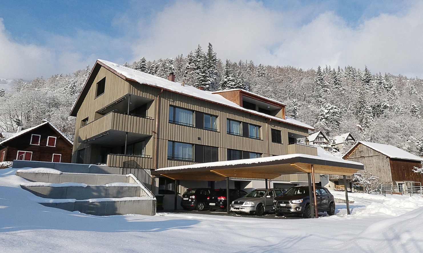 Overall view of the apartment building in Azmoos with shelter for four cars; in winter