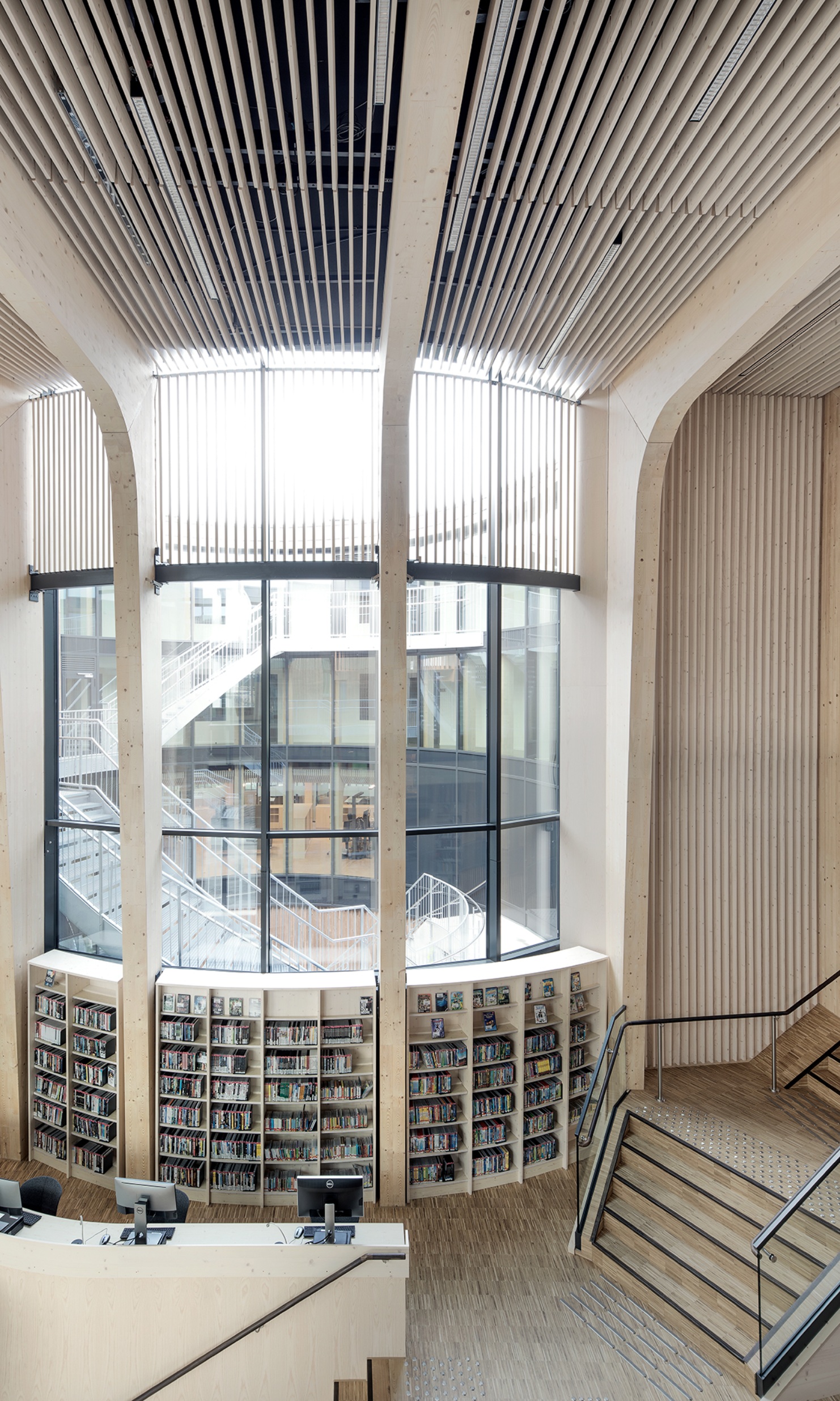 Bibliothèque lumineuse avec escaliers, étagères à livres et grande baie vitrée.<br/>