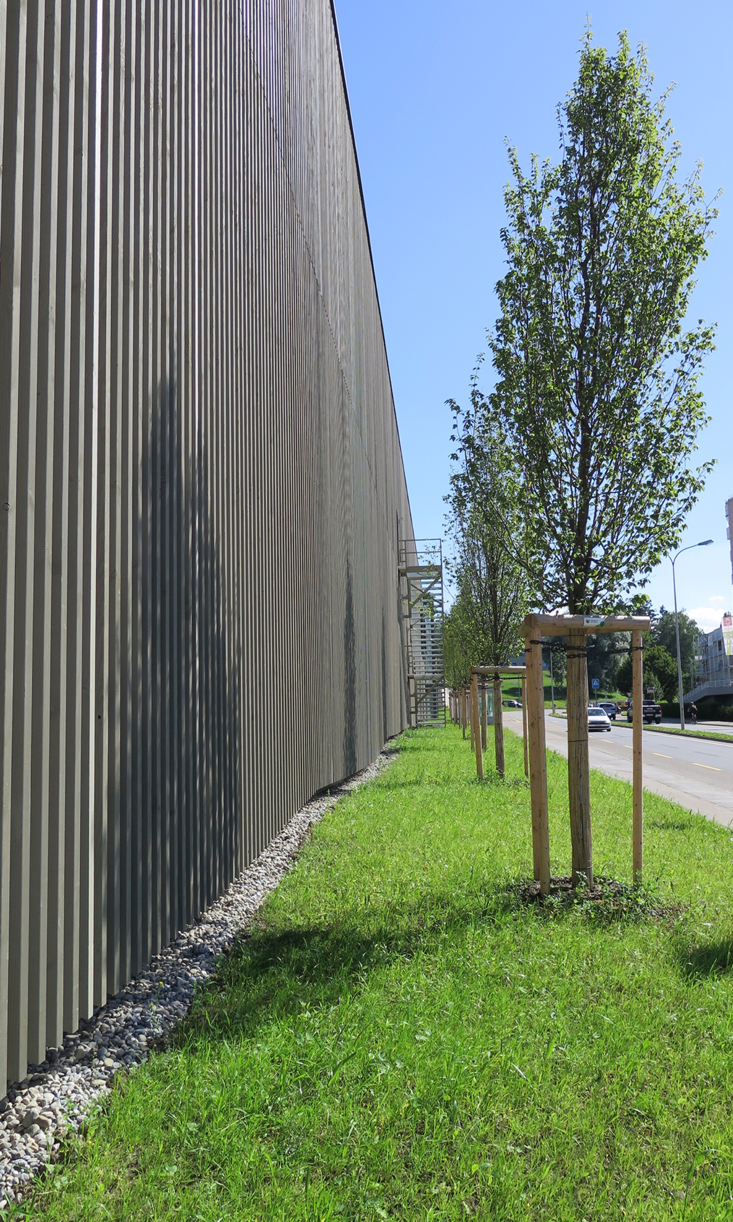 Side view of the Coop Super Center in Uzwil with pre-greyed timber facade and planting.