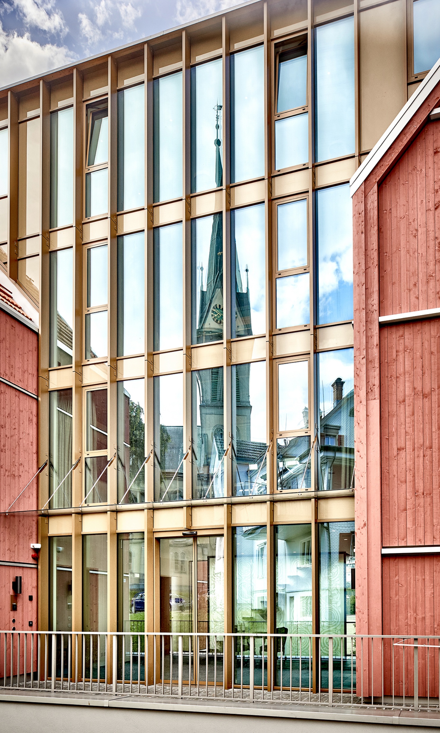 Modern façade with lots of glass, in which the church tower is reflected