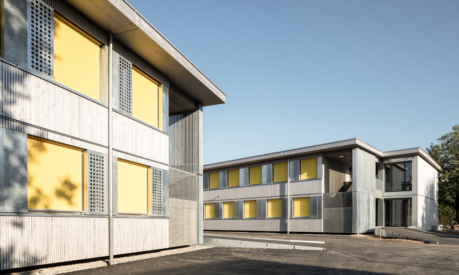 Pavillons scolaire de deux étages avec façades en bois et stores jaunes
