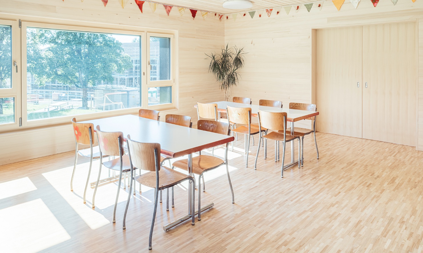 Dining room of the new daycare building. The floor, walls and ceiling of this room are all made of wood, with the large side windows ensuring plenty of daylight.
