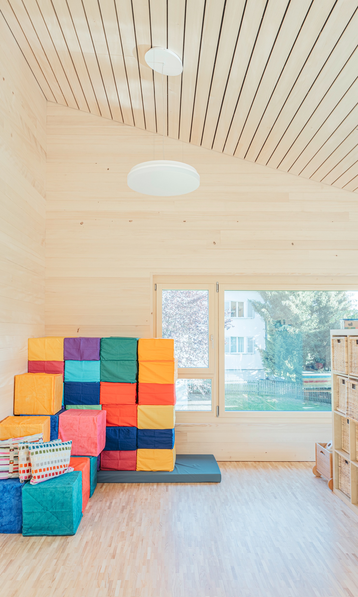 Salle de jeux avec plafond en bois incliné et cubes d’assise colorés empilés