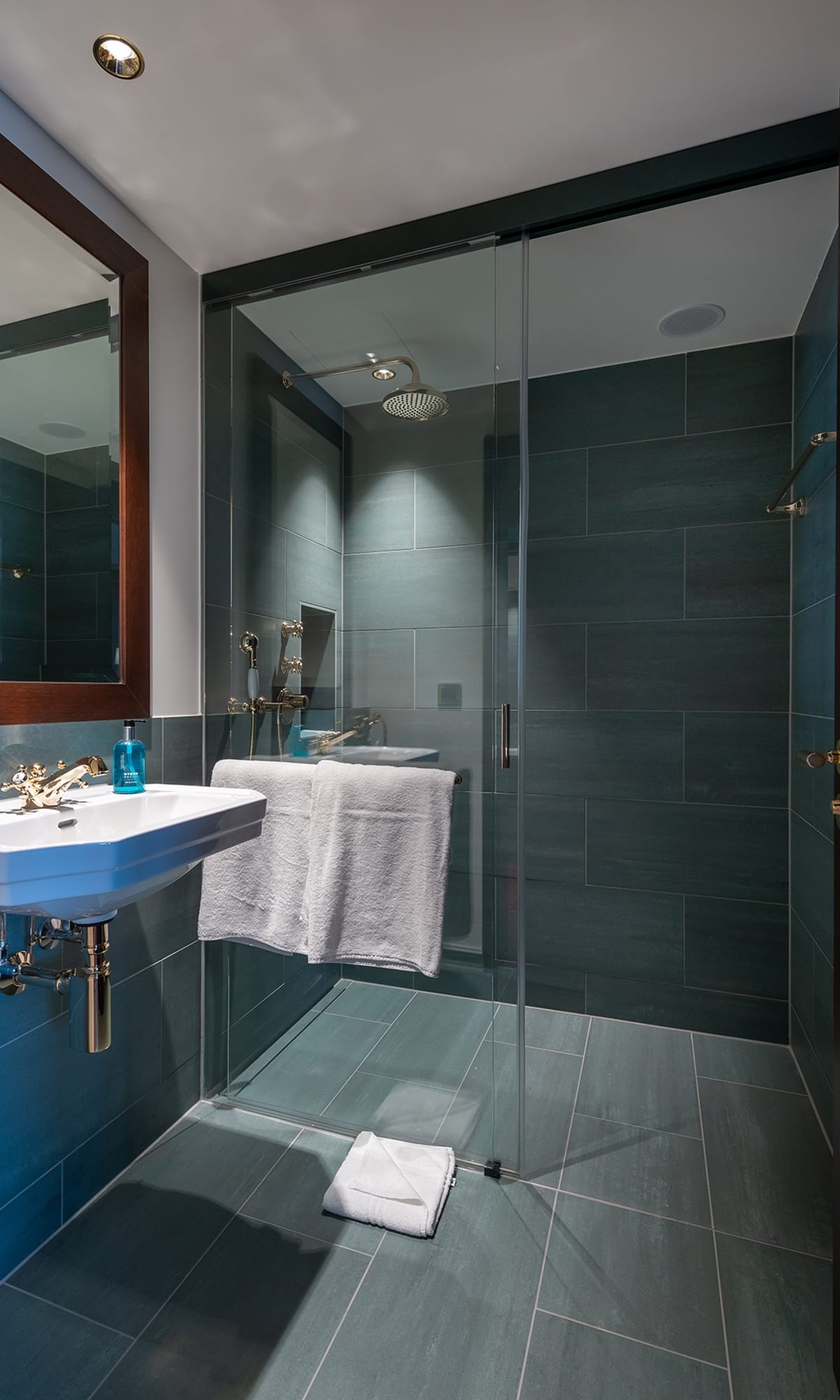 Dusche in einem Gästezimmer des Hotel Bad Horn mit grauen Fliesen und Glastüre und weisses Lavabo <br/><br/>