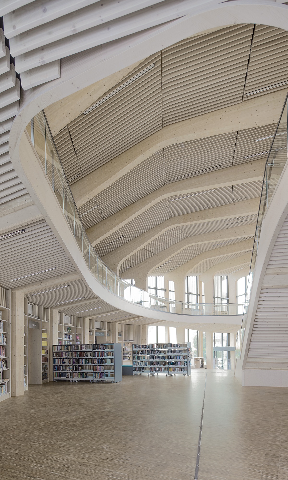 Blick vom Erdgeschoss mit Bücherregalen zum Dach im Bibliotheksgebäude mit auffälliger Holzbauweise.