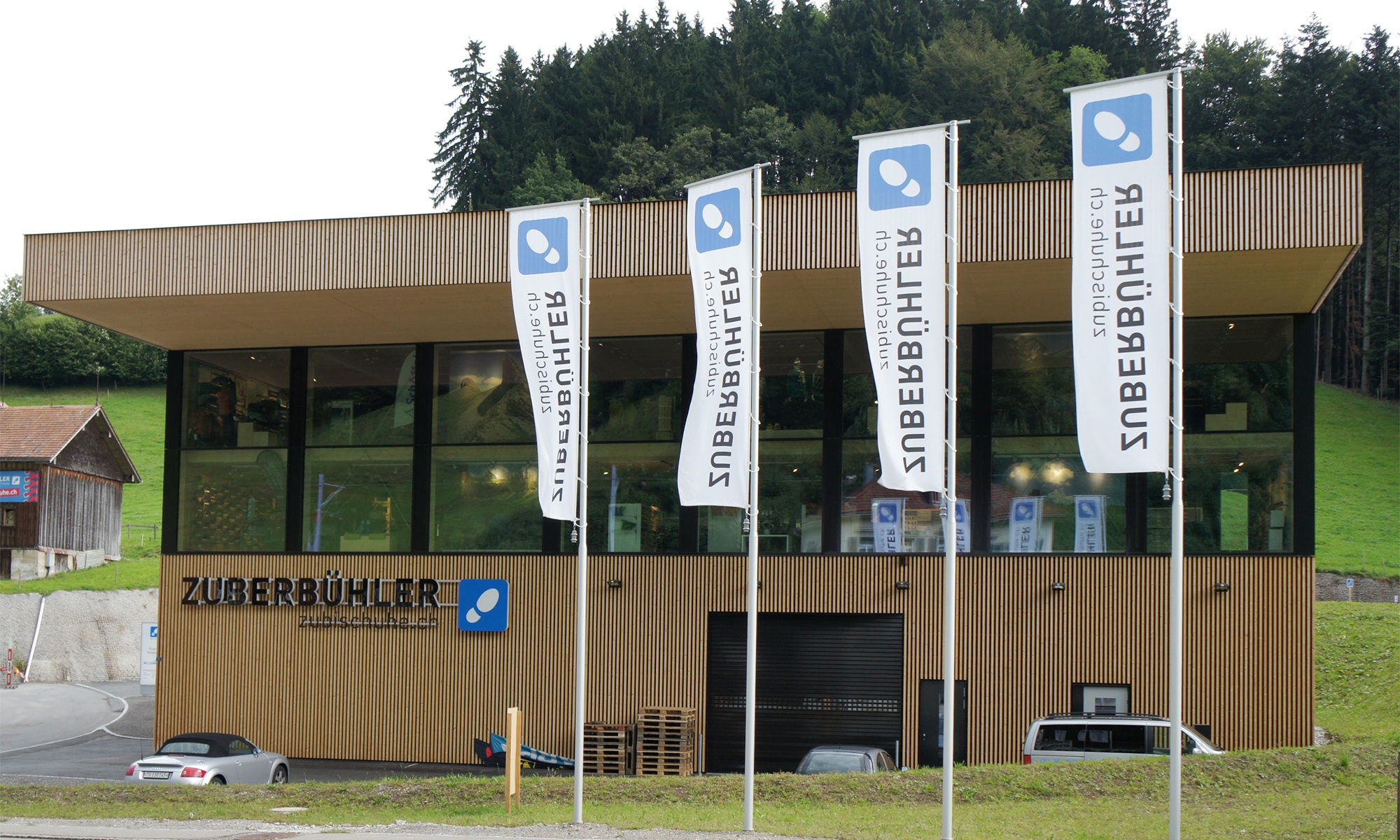 Vue extérieure du bâtiment industriel de Zuberbühler à Herisau avec des drapeaux au premier plan.