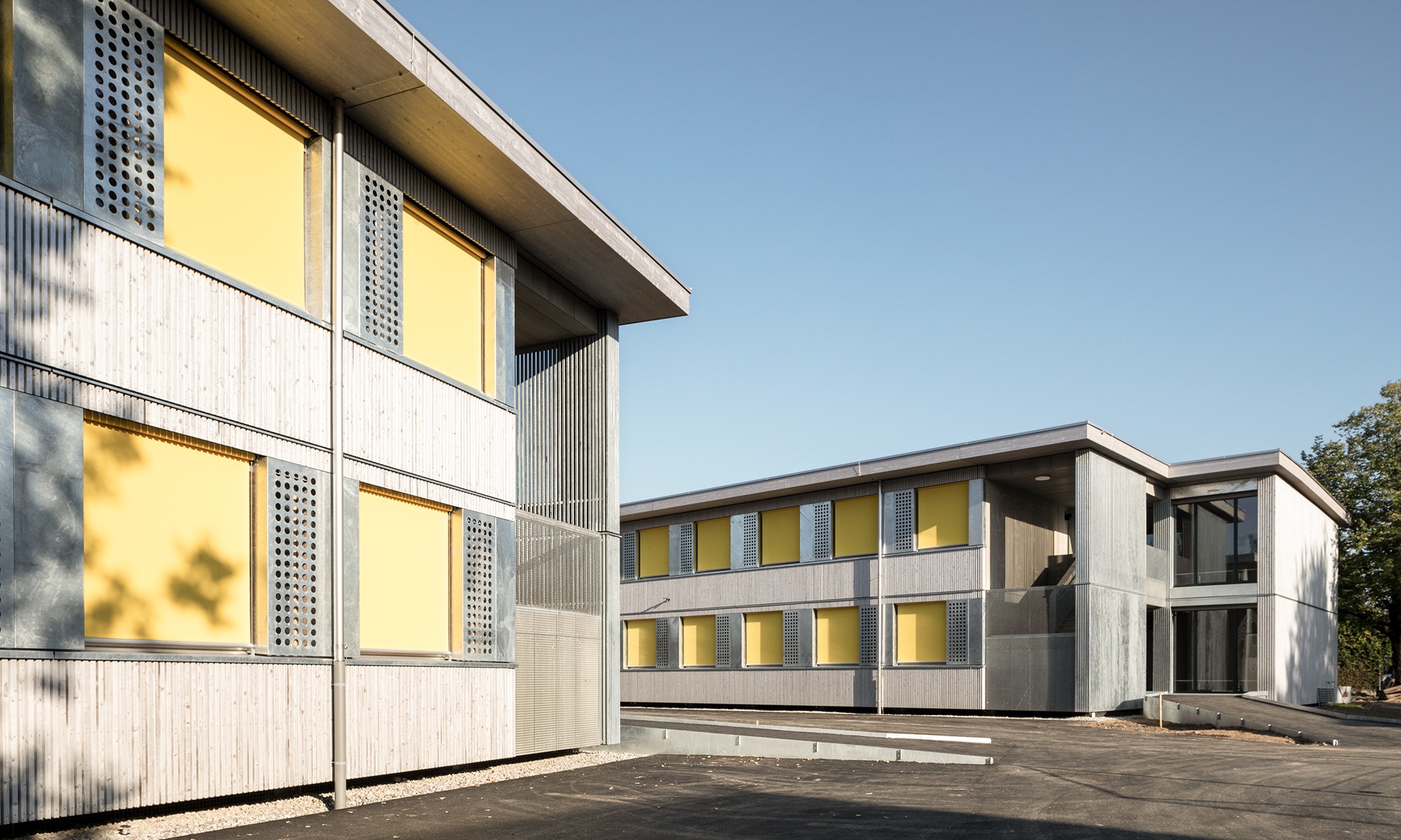Zweigeschossige Schulpavillons Brünnen mit Holzfassaden und gelben Rollläden