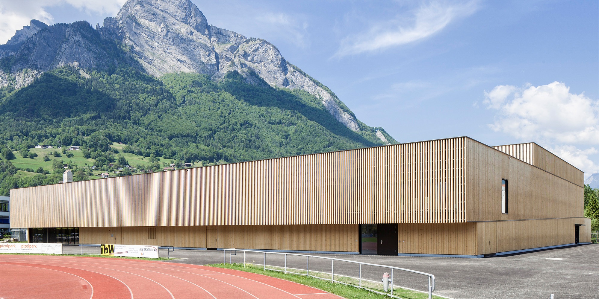 Salle de sport du RSA Sargans avec piste de tartan au premier plan et massif montagneux en arrière-plan.