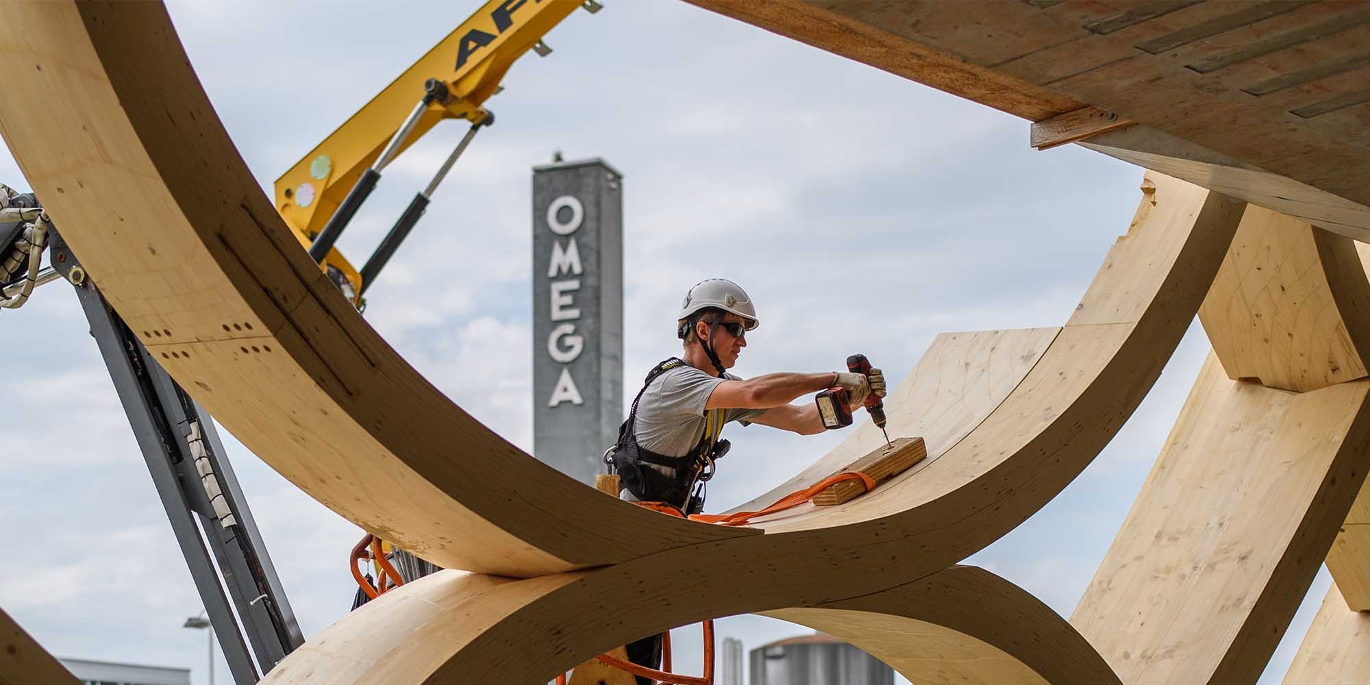 Der Montagemitarbeitende bohrt ein Loch in die Holzkonstruktion des Swatch-Gebäudes