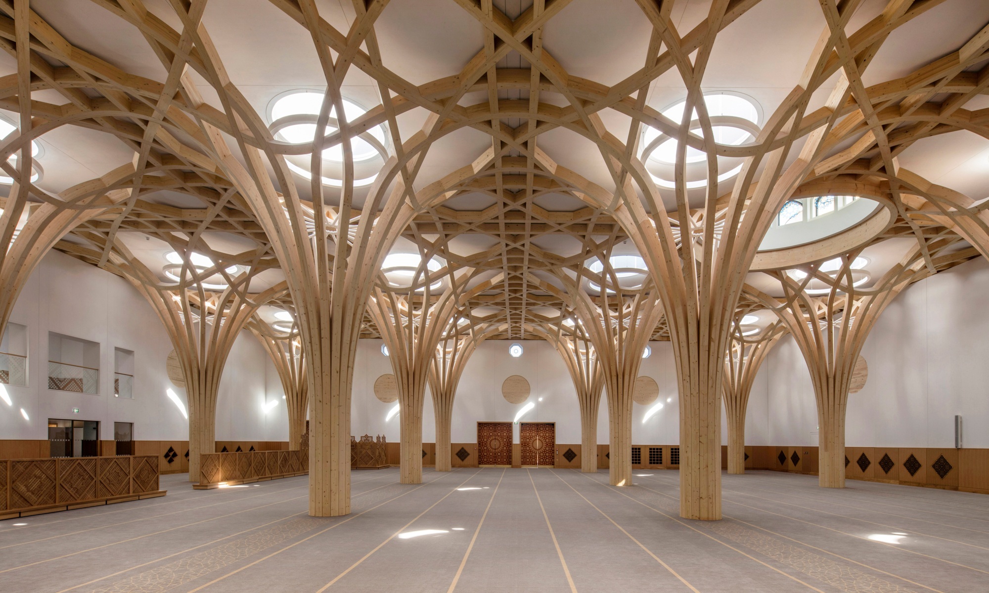 Baumartige Tragstruktur aus Holz und orientalische Holzelemente an Wänden und Türen im Innenbereich der Cambridge Mosque.