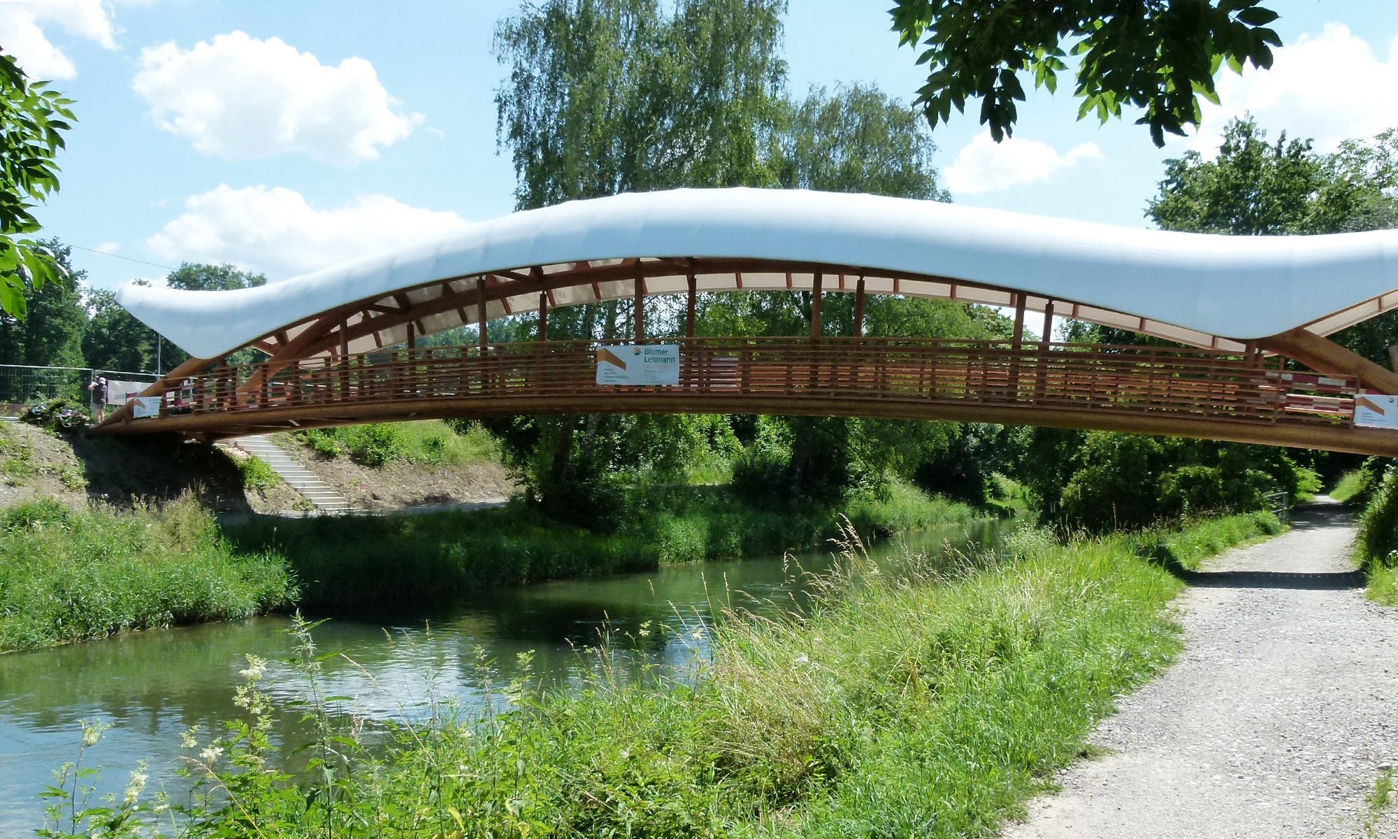 Overall view of the Aubrugg timber art bridge with white curved canopy in fine weather