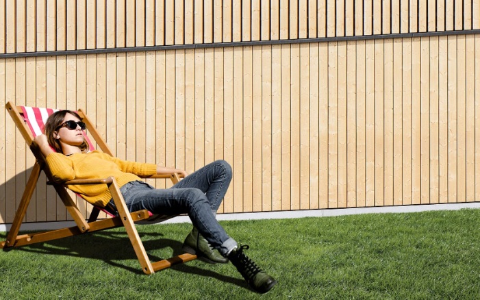 Vacances commerciales 2022 - Jeune femme allongée dans une chaise longue devant un mur en bois 