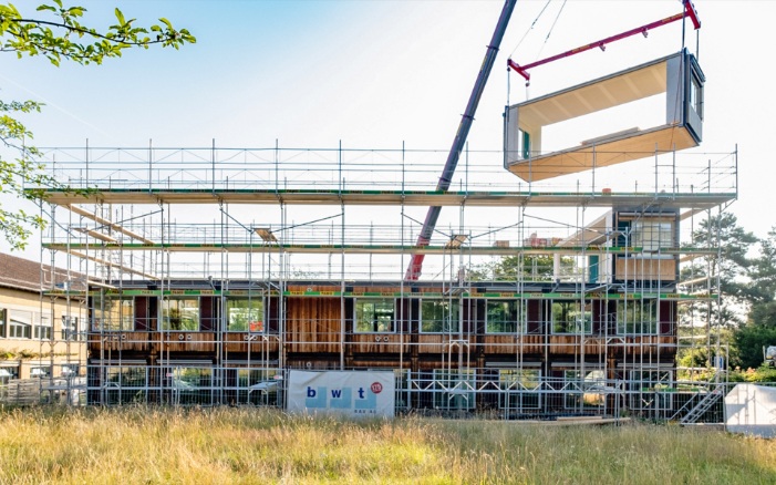 Le bâtiment modulaire ZM10 de l’école de Friesenberg est agrandi d’un étage supplémentaire. Un module en bois est placé sur le toit à l’aide d’une grue. 