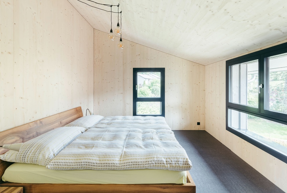 Vue intérieure de la chambre à coucher avec un lit en bois, une longue baie vitrée et une fenêtre individuelle étroite
