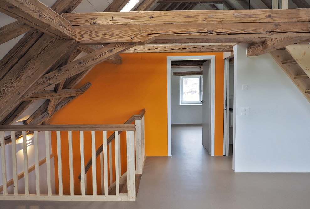 The photograph shows the spacious attic with access to other rooms, two staircases finished entirely in wood and the wide wooden beams.