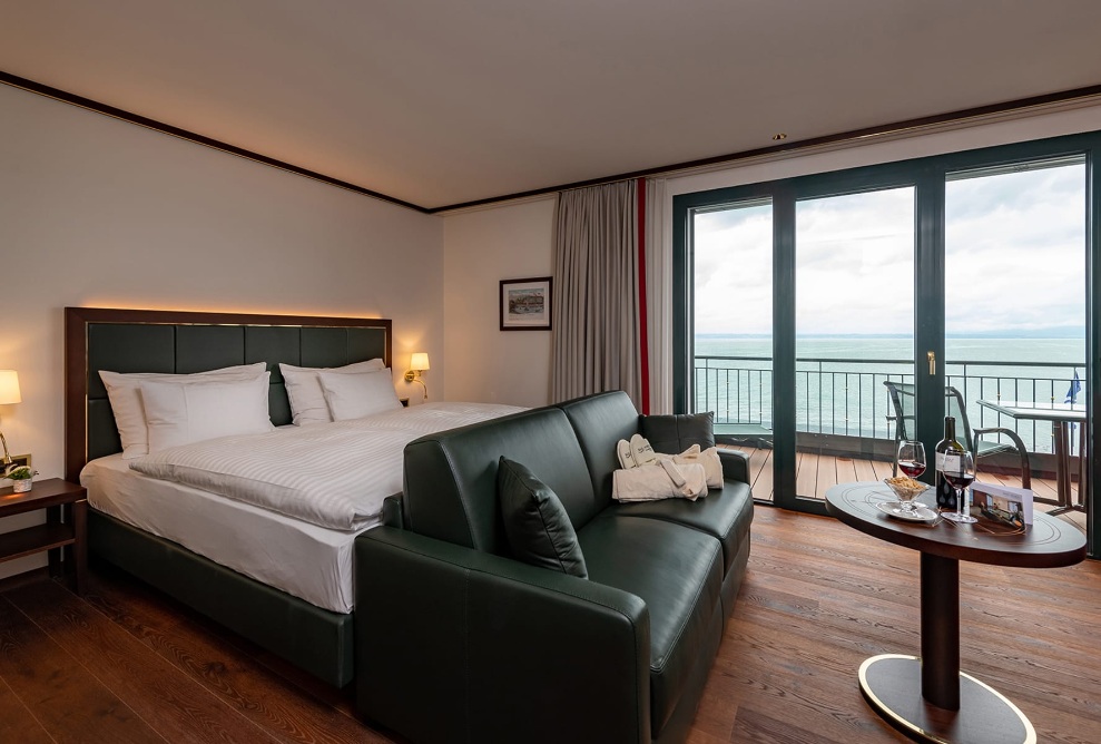 View of a guest room at Hotel Bad Horn with a double bed, large windows and a balcony overlooking Lake Constance