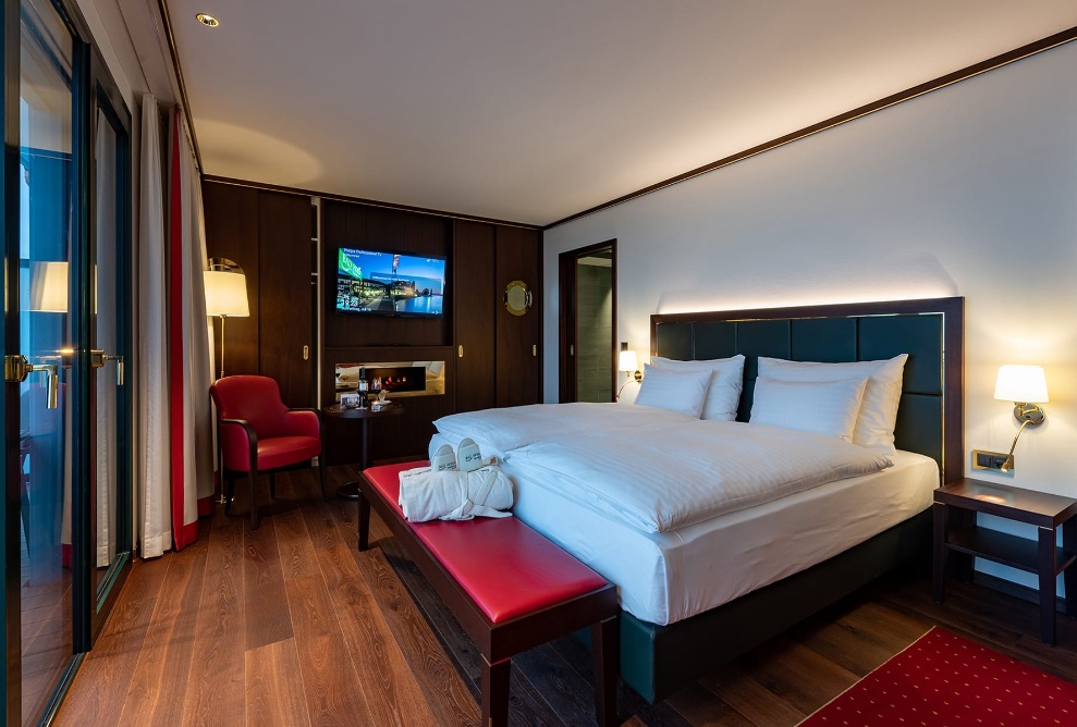 Vue intérieure d’une chambre d’hôtel à l'hôtel Bad Horn avec un lit double, un placard sombre en arrière-plan et une banquette rouge.
