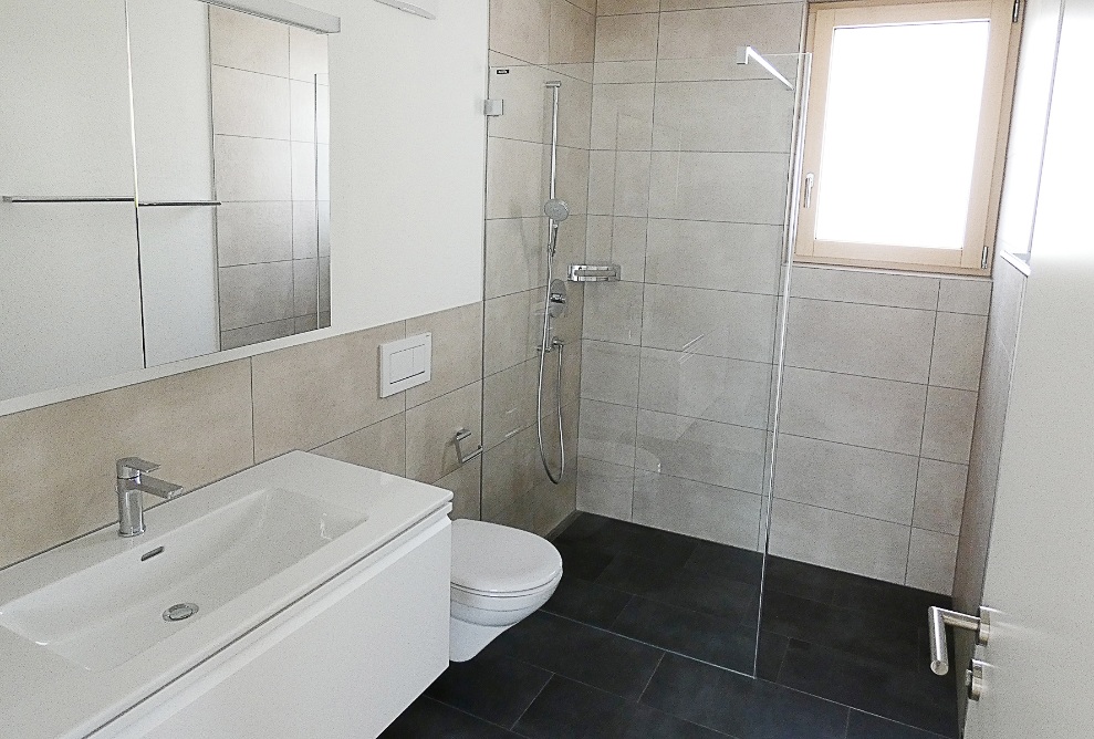 View of the modern bathroom with a black panelled floor, sand-coloured walls and a white suite 