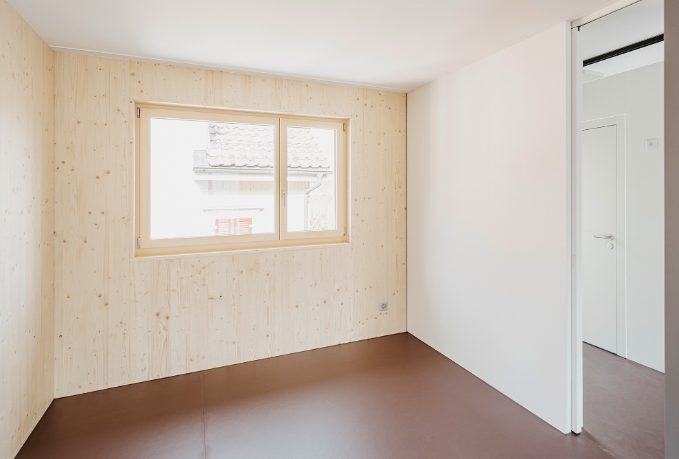 Chambre lumineuse avec fenêtre et murs en bois dans le micro-appartement