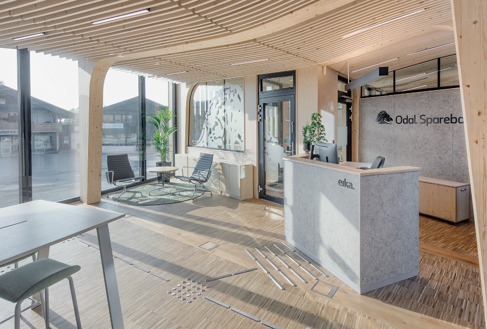 Bright space with stripped-back interior finishing in timber and large windows, equipped with a reception desk and reading corner