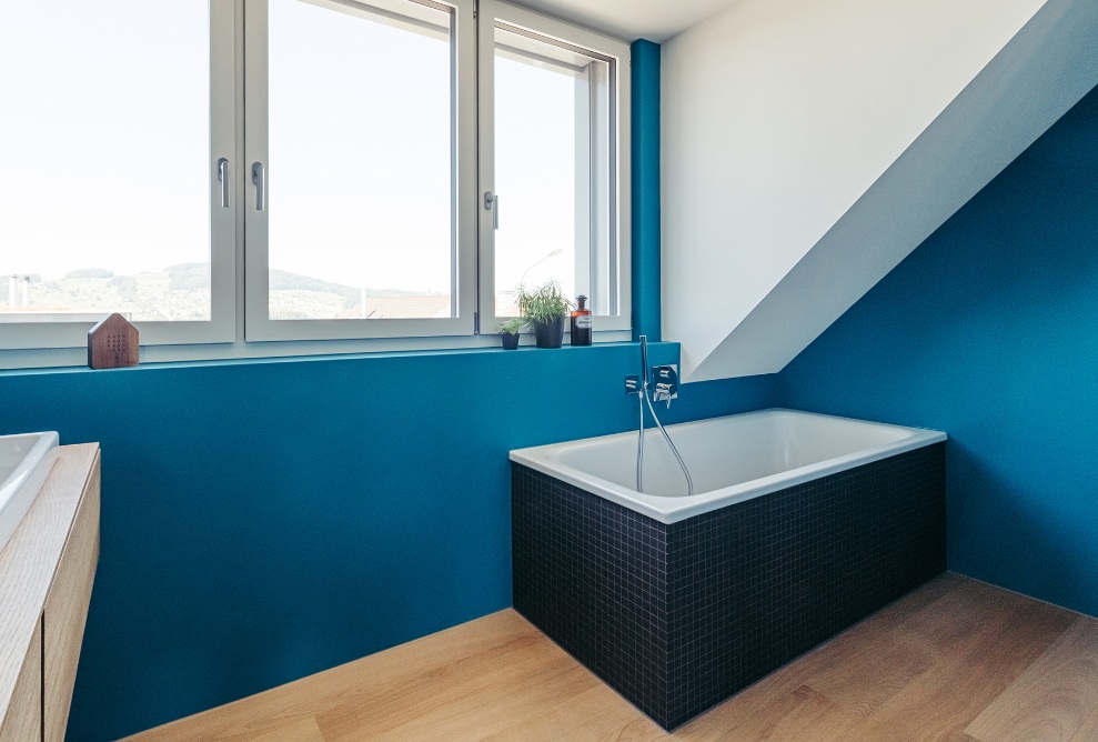 Gesamtansicht des Badezimmers mit blauen Wänden, Holzboden und grosser Fensterfront