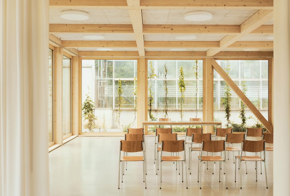 View inside the bright lecture room in the St. Gallen botanical garden, with wooden chairs and a glass wall in the background.