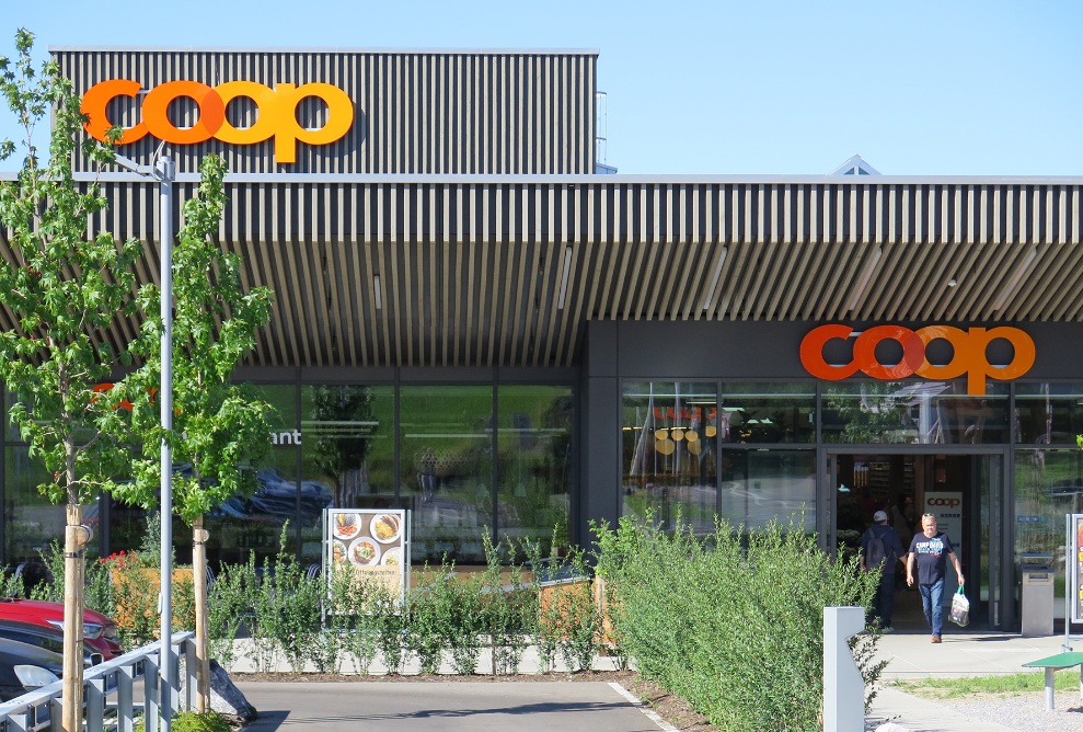 Main entrance of the Coop Super Center in Uzwil with pre-greyed timber facade, forecourt and surrounding area.