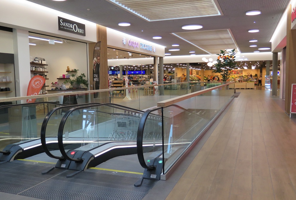 Escalators et magasins dans la zone d’entrée du Coop Super Center Uzwil avec un plancher en bois clair.