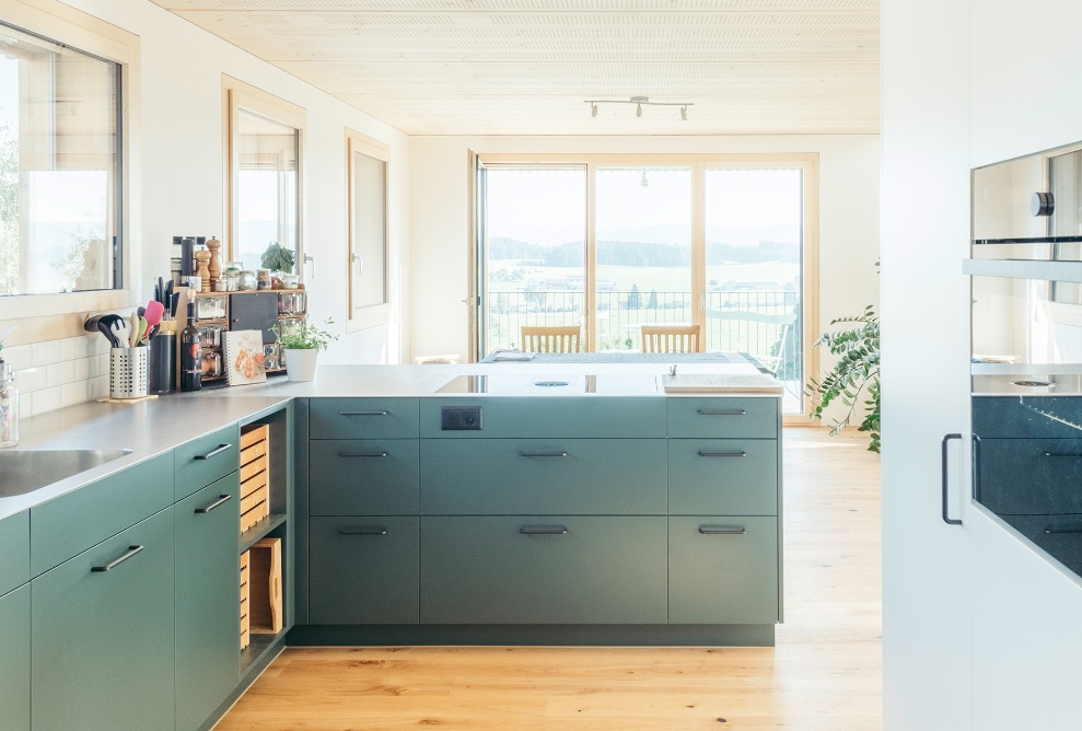 La cuisine moderne aux façades gris-vert est ouverte sur la salle à manger avec balcon.