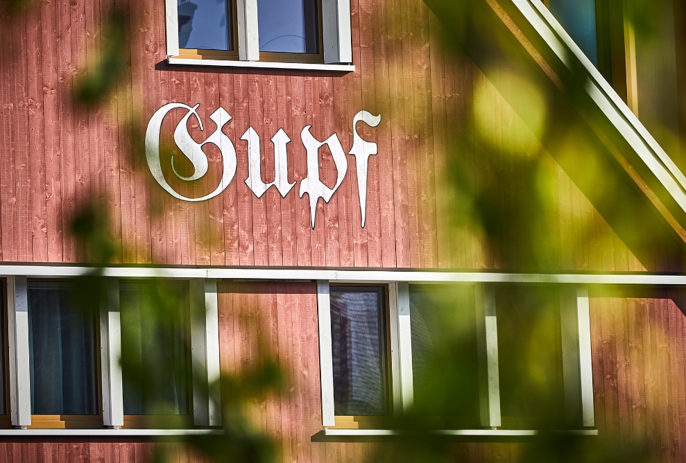 The façade of the Dorfhus Gupf is made of red lacquered spruce wood with white window frames