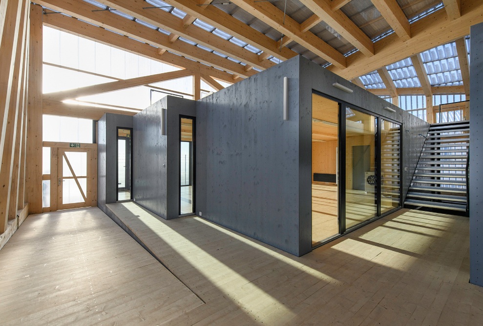 Raumgrosse Holzmodule definieren Raumeinheiten in einer Holzhalle.