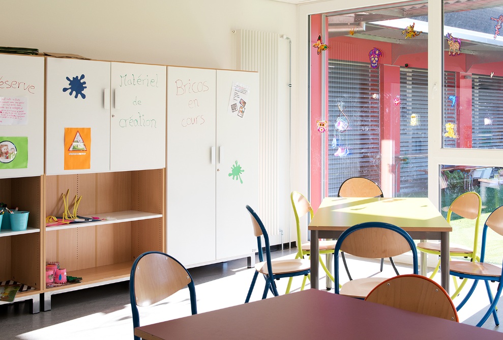 The bright lounge area is finished with wall cabinets decorated with writing and images. The chairs and tables provided offer views of the garden.