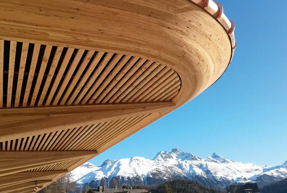 Timber construction against a blue sky with mountains in the background.