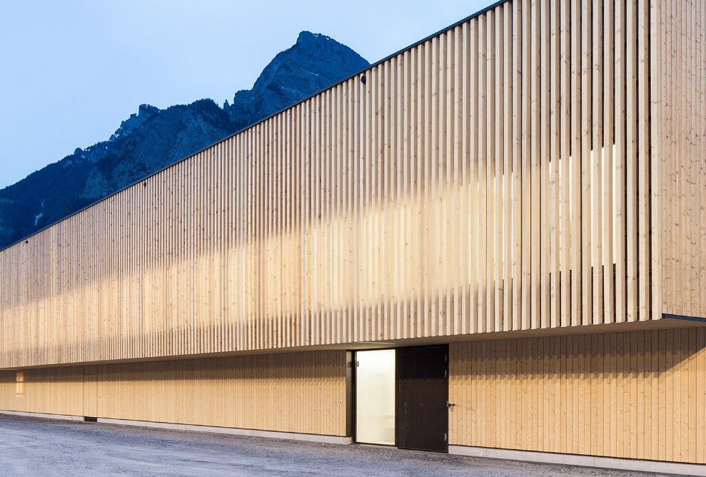 The modern timber construction for RSA Sargans against a mountain backdrop at dusk.